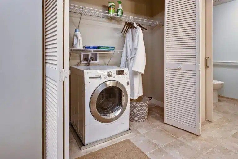 A white washing machine is in a small laundry room  at The Piper, Kansas City, KS.